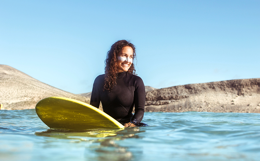 Mujer surfeando en el mar, lleva puesta crema solar en el rostro. Para el artículo: Hablamos sobre protectores solares con cuatro expertas.